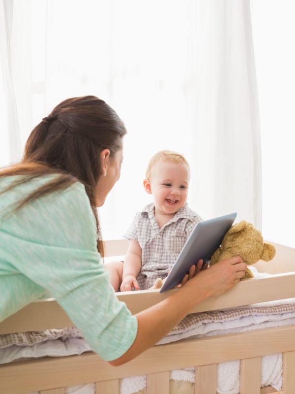 Happy mother using tablet with his baby boy at home in bedroom