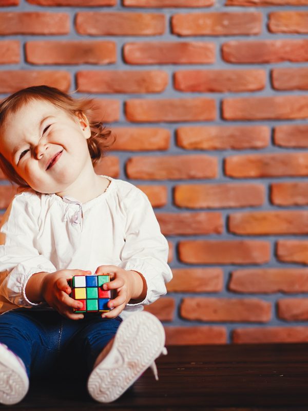 Cute little girl sitting in a room. Child have fun at home near wall. Little girl is studying a colorful cube