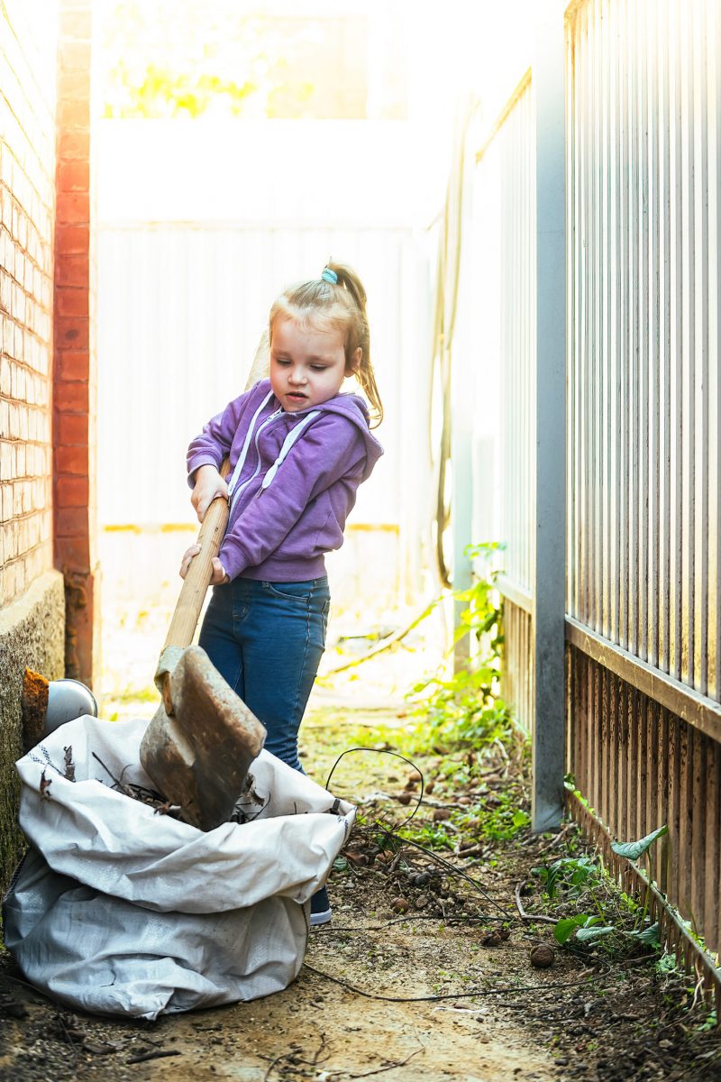 little-girl-helps-adults-she-took-shovel-and-removes-garbage-leaves-in-the-yard-of-the-house