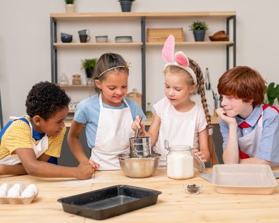 Children wearing apron browsing Internet on digital tablet in order to find recipe of appetizing cookie