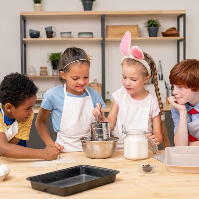 Children wearing apron browsing Internet on digital tablet in order to find recipe of appetizing cookie