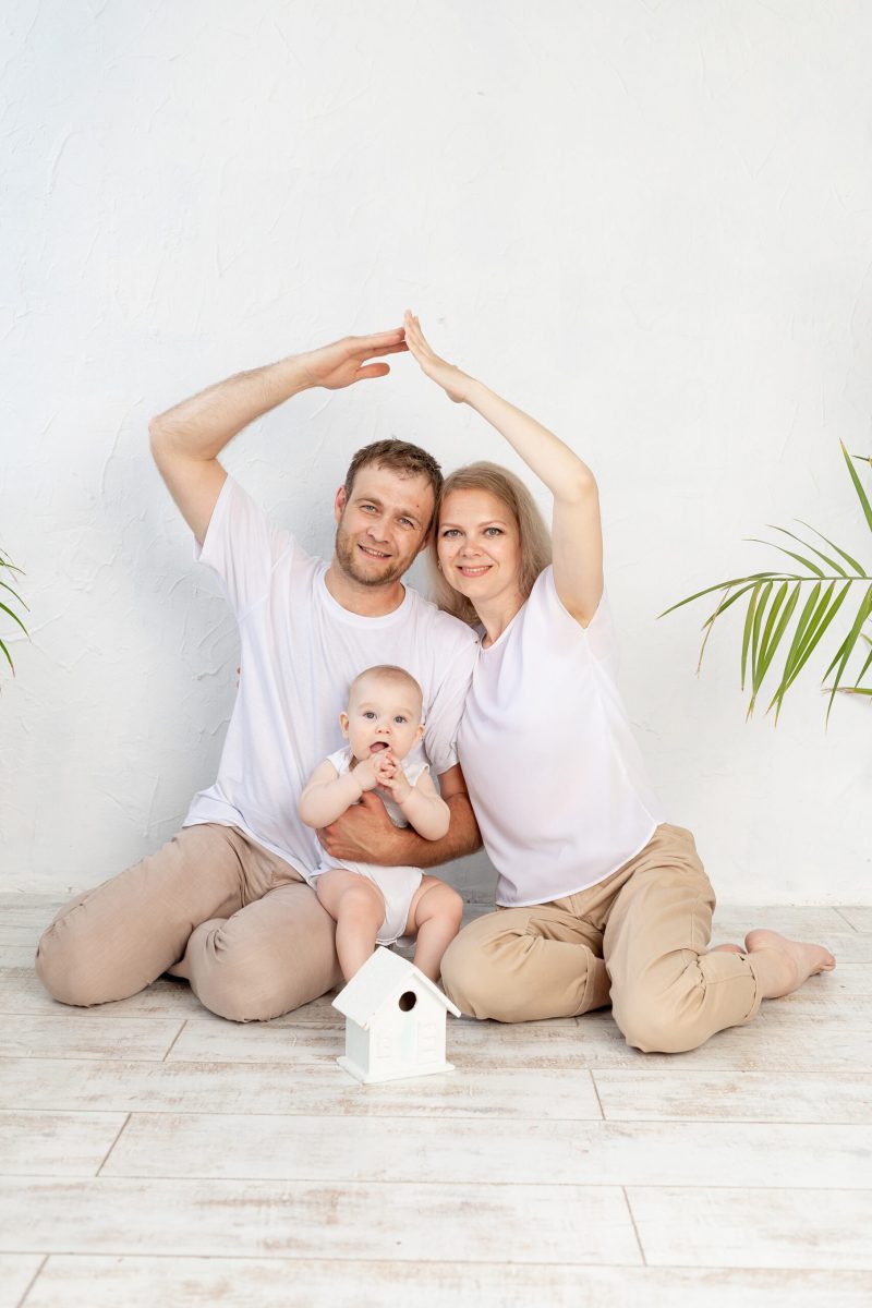 the concept of housing or mortgages for a young family. The mother and father made a roof out of their hands holding the baby in their arms